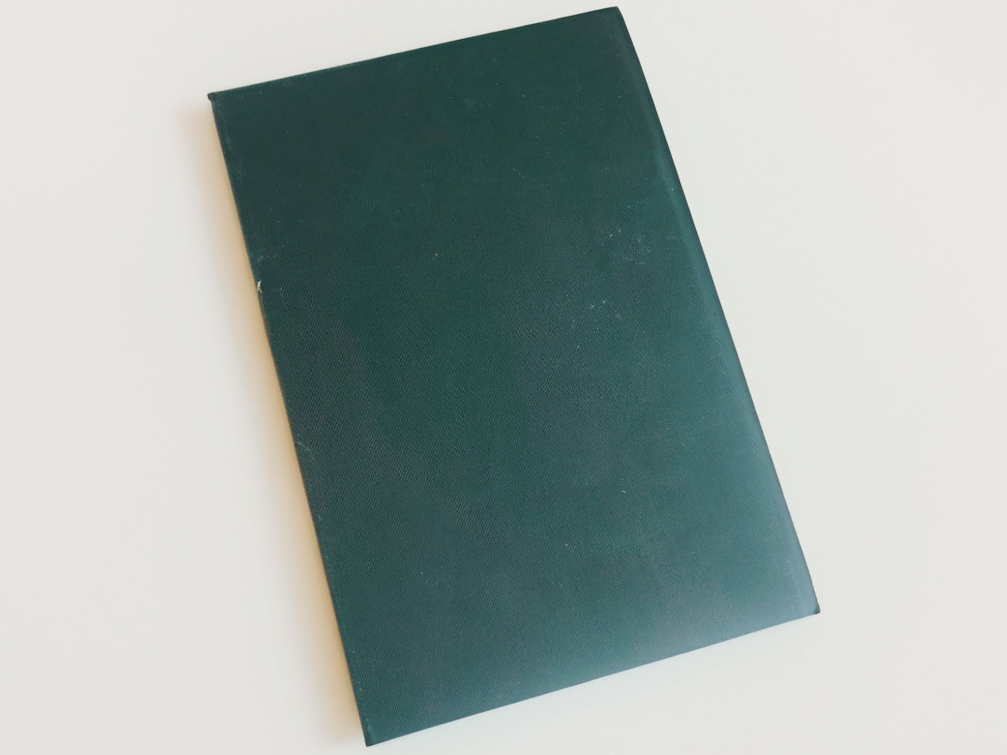 The back of a journal, it is forest green and sits on a white table.